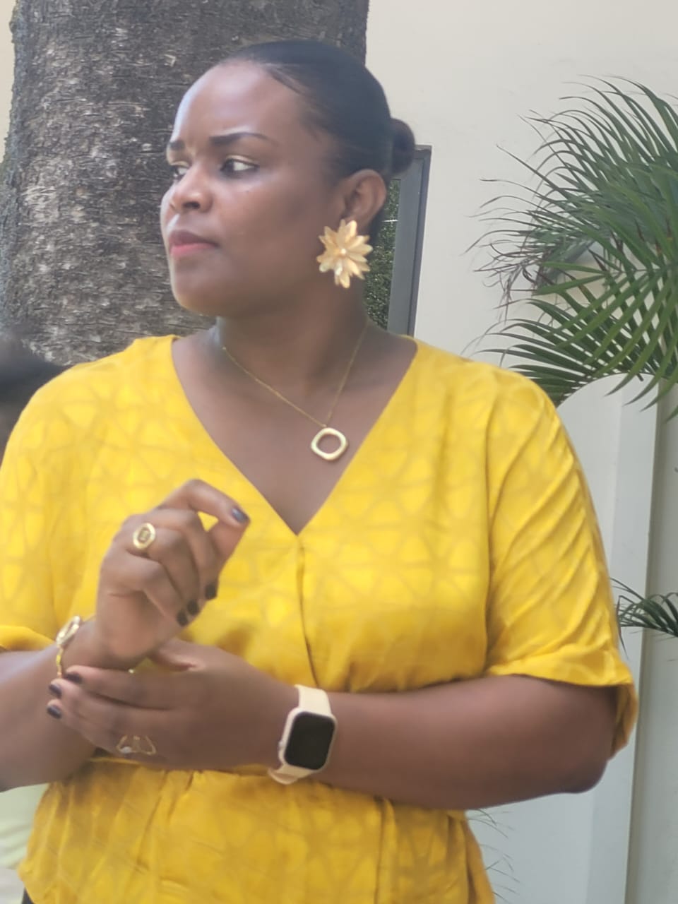 EXL staff member in a yellow blouse standing by a palm tree