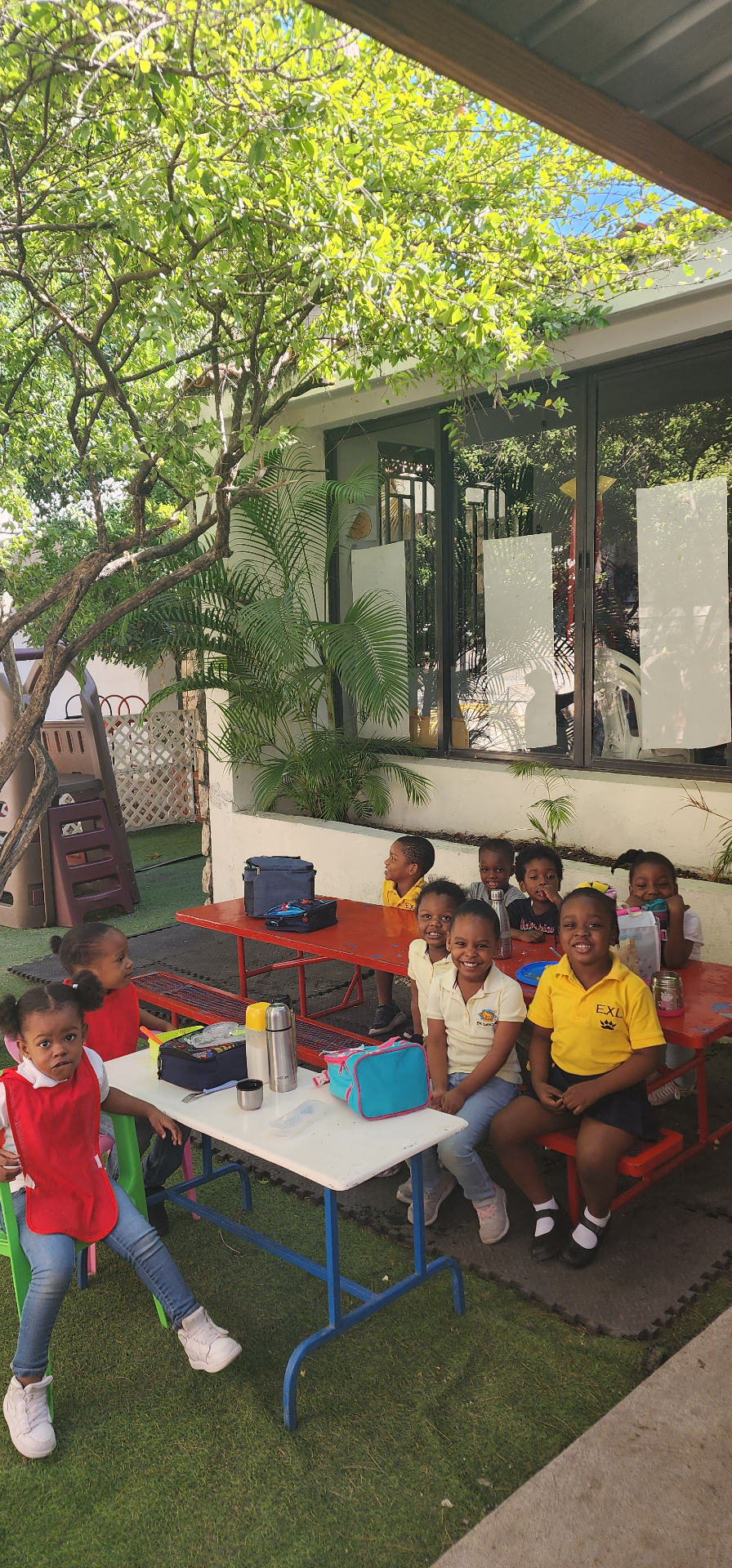Preschool students in EXL uniforms sitting at outdoor picnic tables during lunch