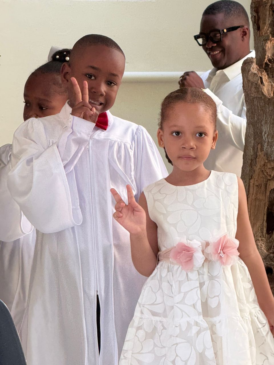 Young EXL graduate in white gown flashing peace signs with a friend