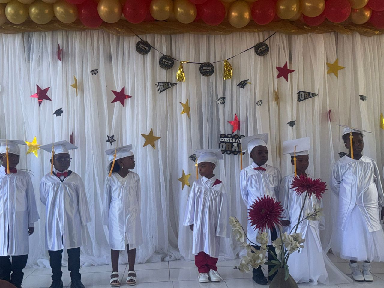 EXL preschool graduates in white caps and gowns on stage