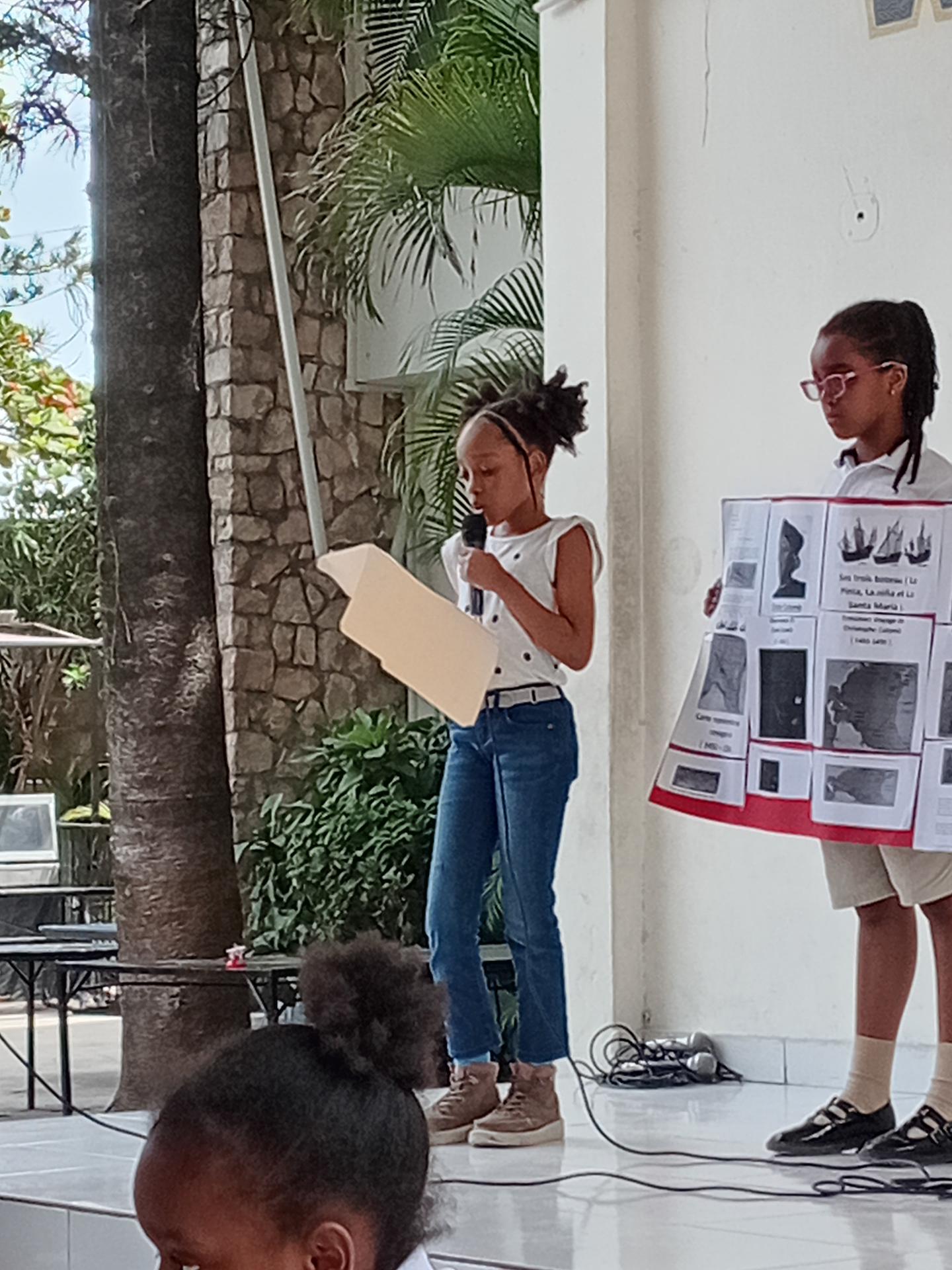 EXL students presenting a history project on stage with a visual poster